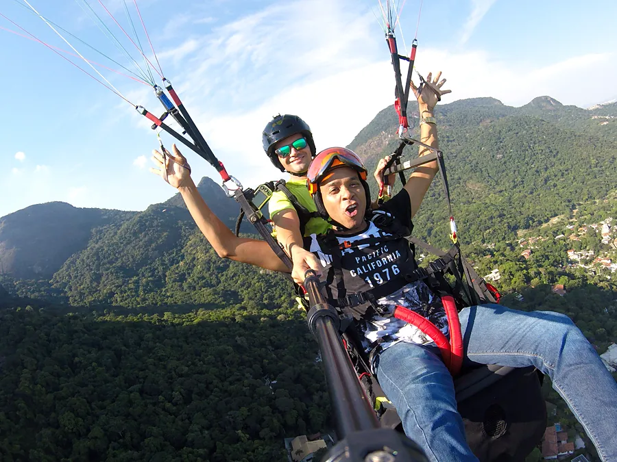 Passageiro animado em voo de parapente com a Pedra da Gávea e a floresta ao fundo