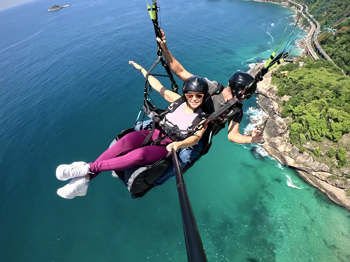 Pés de passageira no ar com a Praia de São Conrado lá embaixo durante voo de parapente
