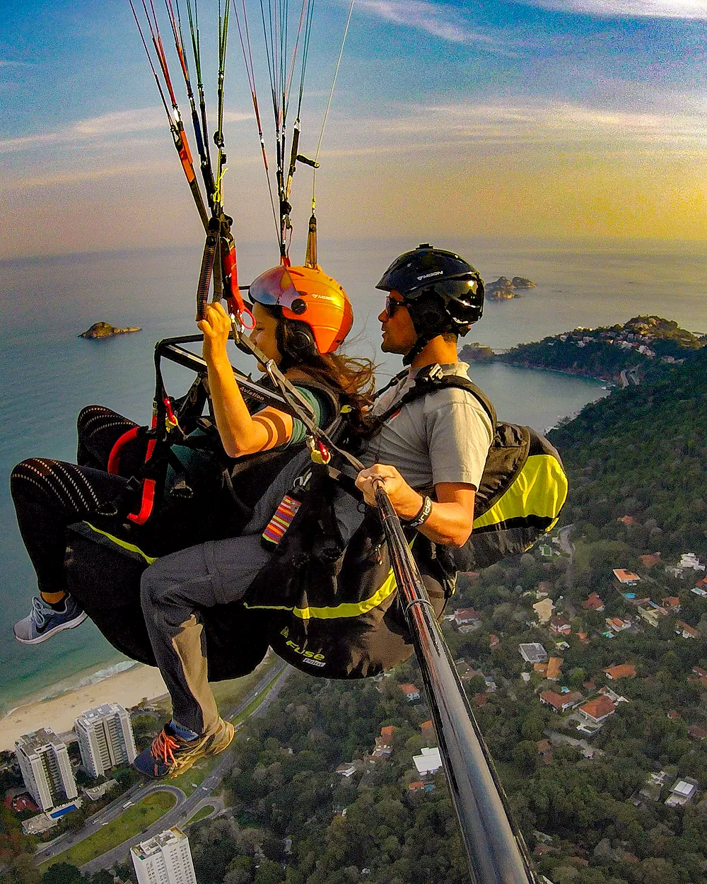 Passageira e piloto em voo de parapente ao pôr do sol sobre São Conrado