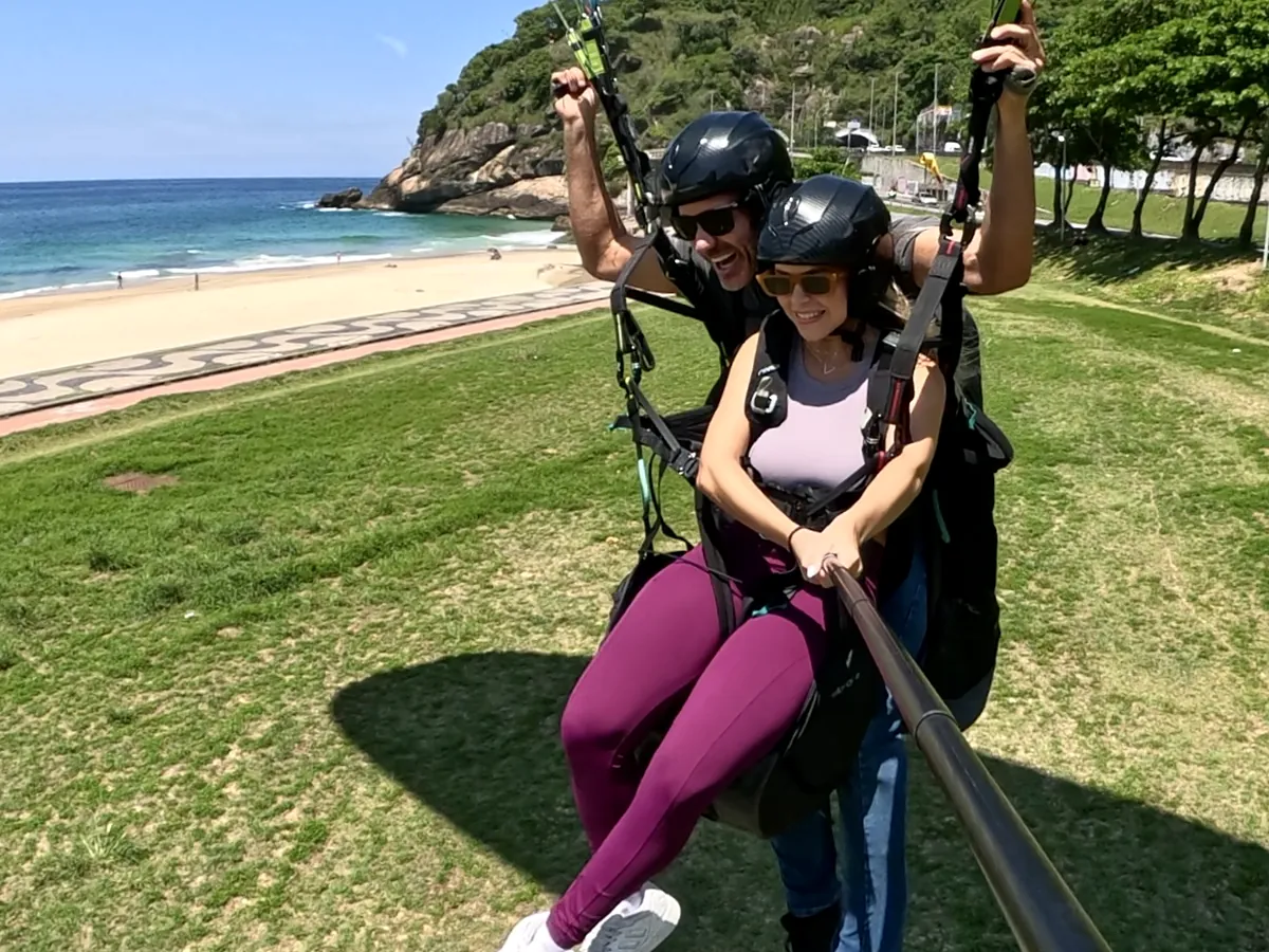 Passageira sorrindo com o piloto logo após o pouso de parapente em São Conrado