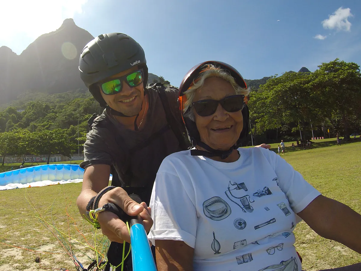 Senhora sorridente ao lado do piloto antes do voo duplo de parapente no gramado de São Conrado