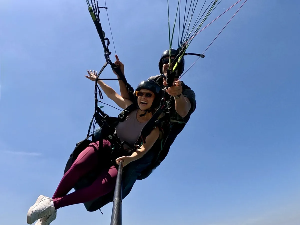 Passageira sorrindo em voo de parapente sobre o mar azul de São Conrado